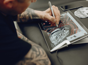 A tattooed man drawing a design on a tablet